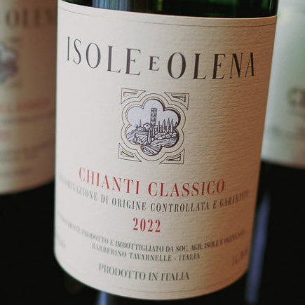 Wine bottles with labels, including 'Tsole e Olena' Chianti Classico, on a wooden surface.